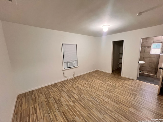 unfurnished bedroom with ensuite bathroom, cooling unit, and wood-type flooring