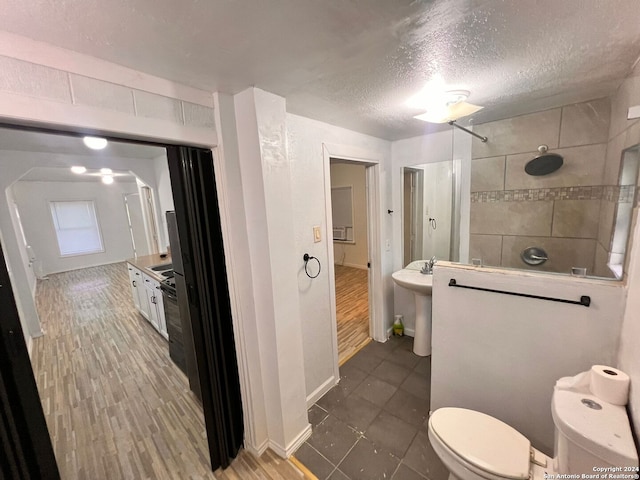 bathroom featuring hardwood / wood-style floors, sink, toilet, tiled shower, and a textured ceiling