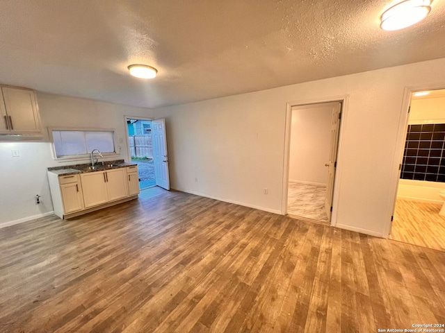 kitchen with a textured ceiling, white cabinets, sink, and light hardwood / wood-style flooring