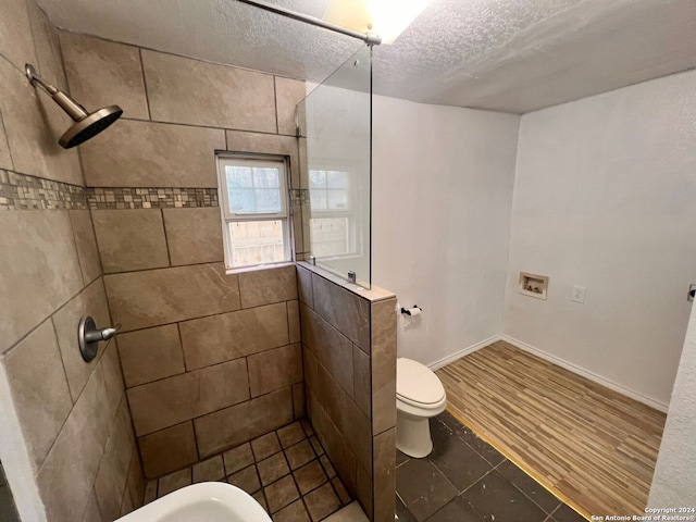 bathroom with a tile shower, a textured ceiling, toilet, and hardwood / wood-style floors