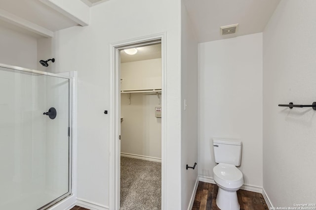 bathroom with hardwood / wood-style floors, toilet, and a shower with door