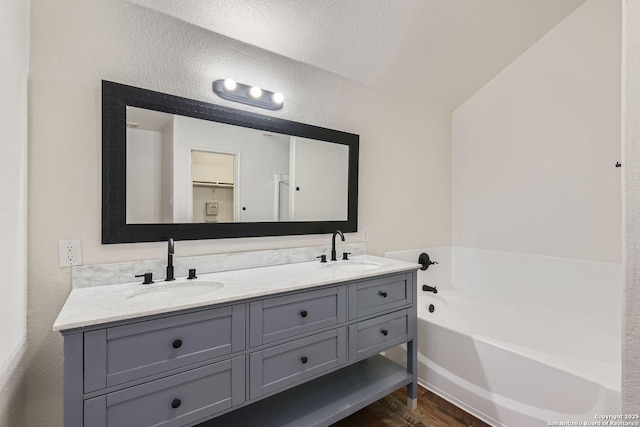 bathroom featuring a bathtub, vanity, a textured ceiling, hardwood / wood-style floors, and lofted ceiling