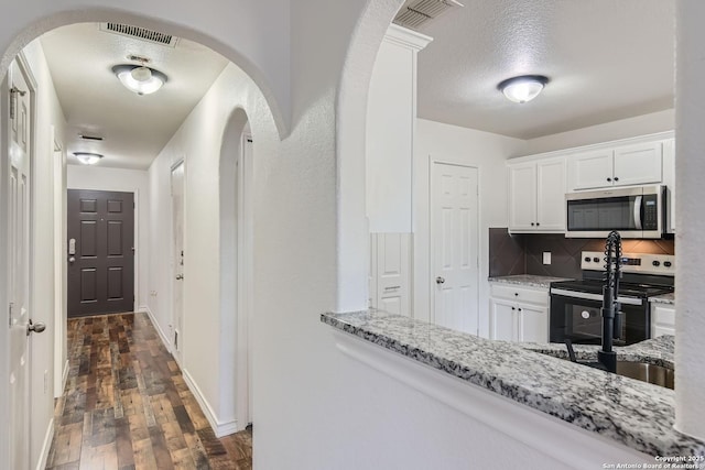 kitchen with light stone countertops, appliances with stainless steel finishes, backsplash, dark hardwood / wood-style floors, and white cabinetry