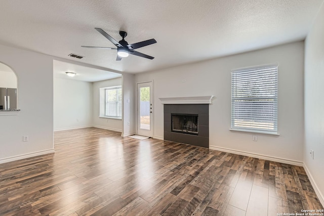 unfurnished living room with a textured ceiling, a tiled fireplace, ceiling fan, and dark hardwood / wood-style floors