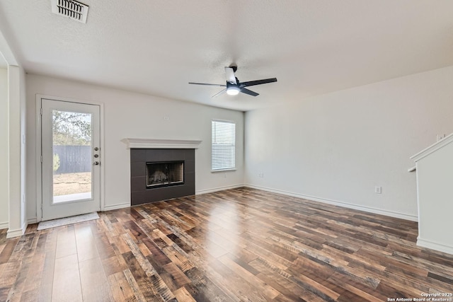 unfurnished living room featuring a tiled fireplace, ceiling fan, dark wood-type flooring, and a textured ceiling