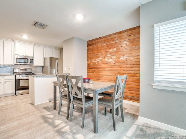 dining room featuring light wood-type flooring and wooden walls