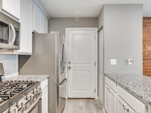 kitchen featuring light stone countertops, white cabinets, light hardwood / wood-style floors, and appliances with stainless steel finishes