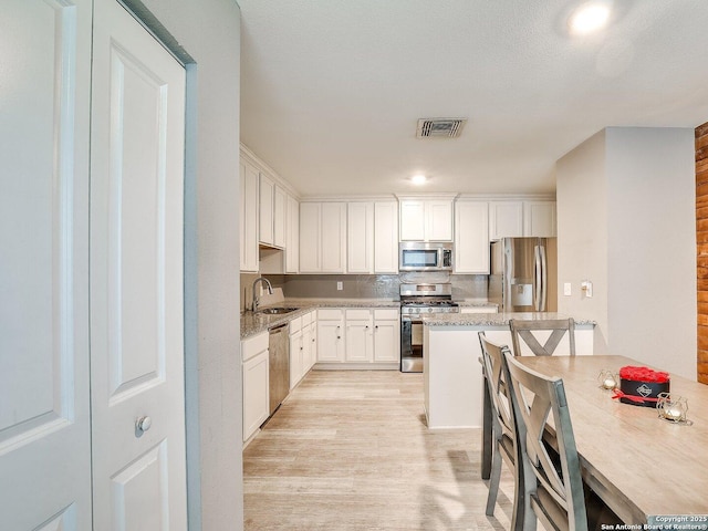 kitchen with backsplash, white cabinets, sink, light wood-type flooring, and stainless steel appliances