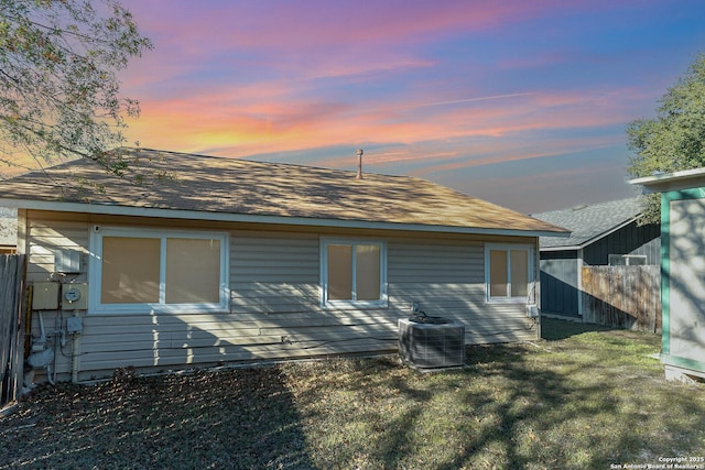 back house at dusk with a lawn and central AC