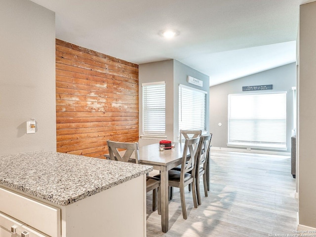 dining room featuring lofted ceiling and wooden walls