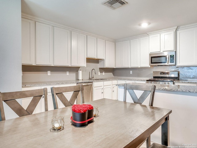 kitchen with white cabinets, appliances with stainless steel finishes, light stone countertops, and sink