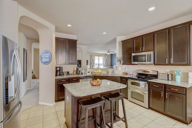 kitchen featuring sink, a center island, a kitchen bar, light tile patterned flooring, and appliances with stainless steel finishes