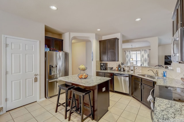 kitchen with dark brown cabinetry, sink, hanging light fixtures, stainless steel appliances, and a kitchen island