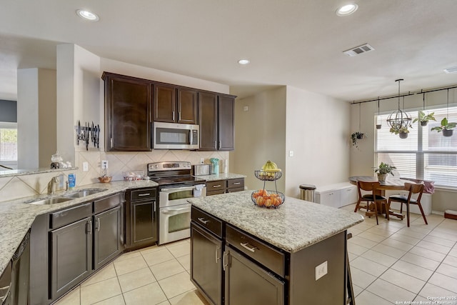 kitchen with hanging light fixtures, light stone countertops, sink, and appliances with stainless steel finishes