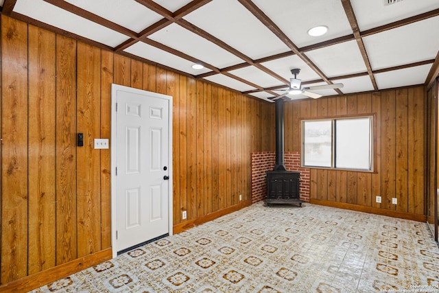 unfurnished living room with ceiling fan, beam ceiling, a wood stove, and coffered ceiling