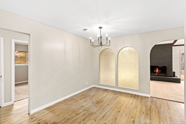 unfurnished dining area with a fireplace, hardwood / wood-style floors, and an inviting chandelier