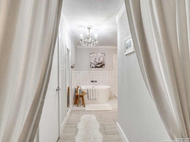 bathroom featuring a washtub, a textured ceiling, crown molding, and a notable chandelier