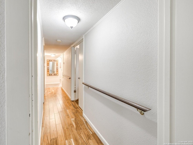 corridor featuring light hardwood / wood-style floors, a textured ceiling, and ornamental molding