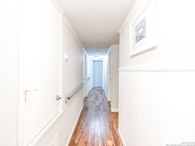 corridor with hardwood / wood-style floors, a textured ceiling, and ornamental molding