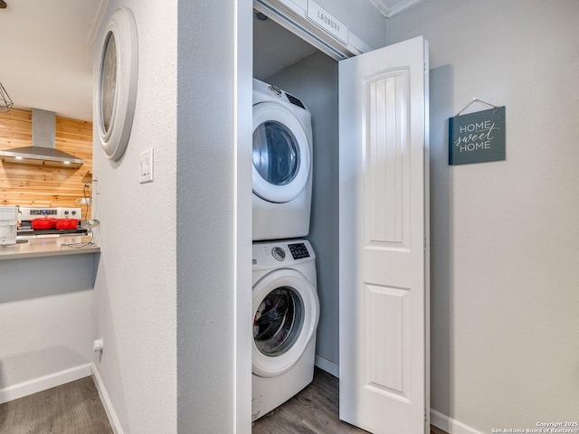 laundry room featuring wood walls, stacked washer and dryer, and wood-type flooring