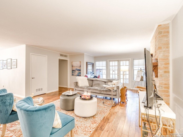 living room featuring a brick fireplace, light hardwood / wood-style floors, ornamental molding, and french doors