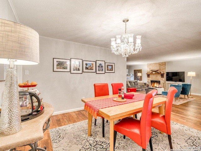 dining space featuring a stone fireplace, ornamental molding, a notable chandelier, a textured ceiling, and light wood-type flooring