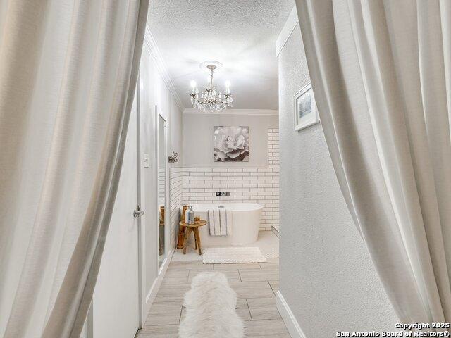 bathroom with a textured ceiling, a washtub, crown molding, and a chandelier