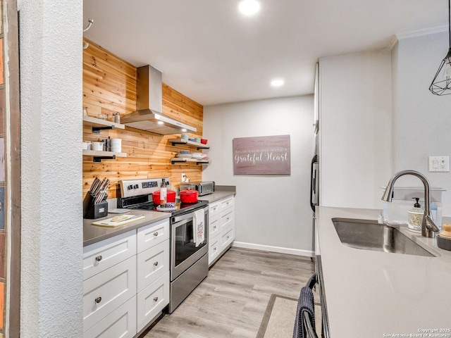 kitchen with wall chimney exhaust hood, stainless steel electric stove, wooden walls, white cabinetry, and hanging light fixtures