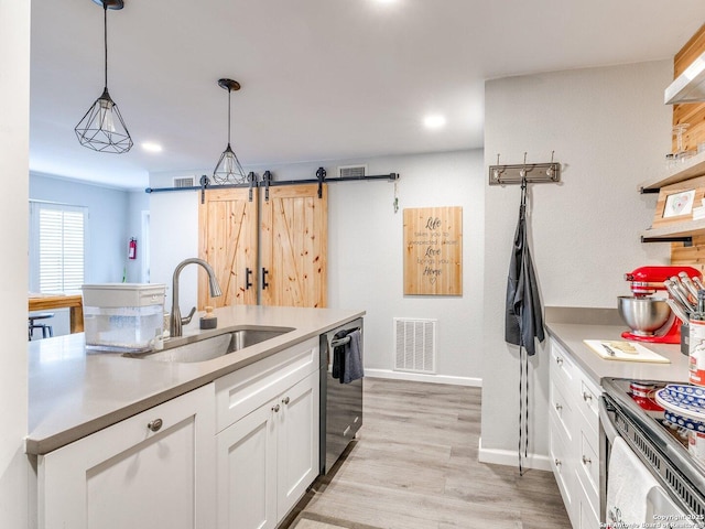 kitchen with stainless steel appliances, sink, pendant lighting, a barn door, and white cabinets