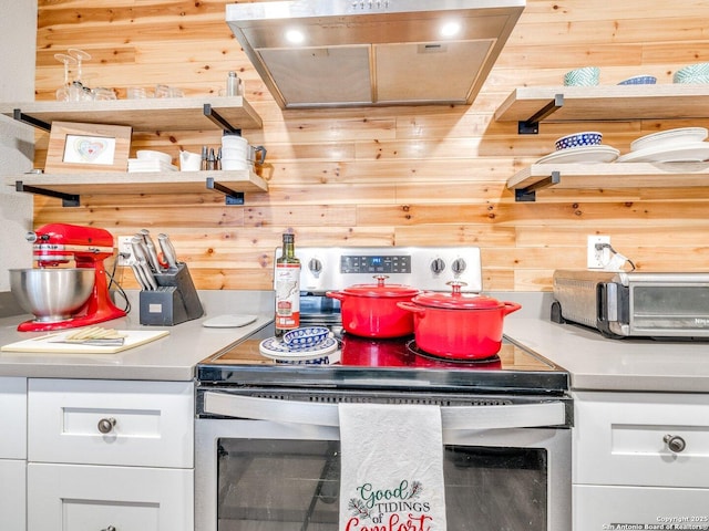 kitchen featuring white cabinetry, wood walls, exhaust hood, and stainless steel electric range