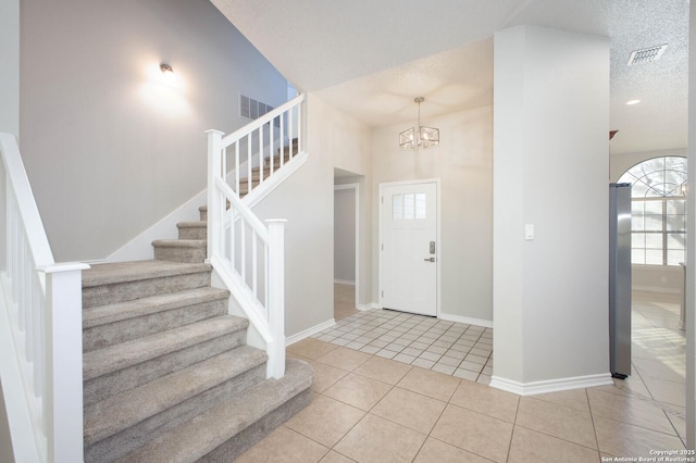 tiled entryway with a textured ceiling and a chandelier