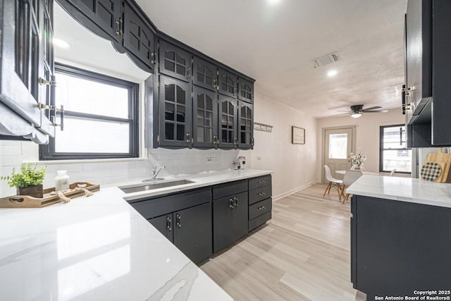 kitchen with ceiling fan, decorative backsplash, light wood-type flooring, and sink