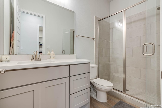 bathroom featuring a shower with door, vanity, hardwood / wood-style floors, and toilet