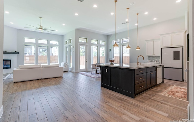 kitchen with plenty of natural light, a kitchen island with sink, ceiling fan, white cabinetry, and hanging light fixtures