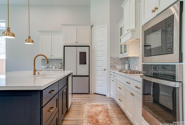 kitchen featuring backsplash, stainless steel appliances, sink, white cabinets, and hanging light fixtures