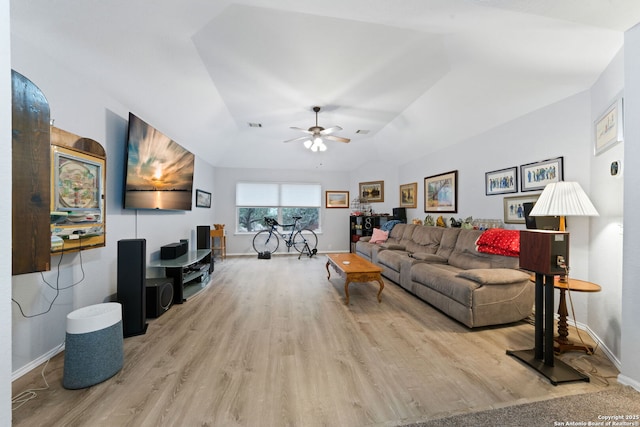 living room with ceiling fan, a raised ceiling, light wood-type flooring, and vaulted ceiling