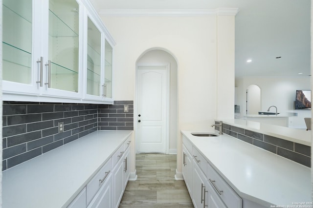 kitchen with sink, crown molding, decorative backsplash, white cabinets, and light wood-type flooring