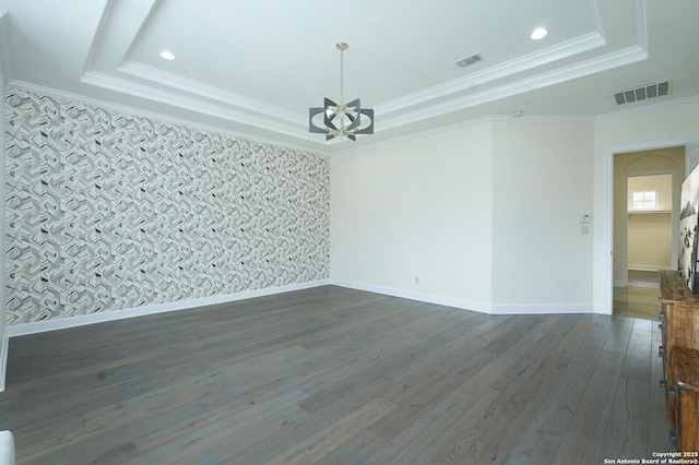 spare room with a raised ceiling, dark hardwood / wood-style flooring, ornamental molding, and a notable chandelier