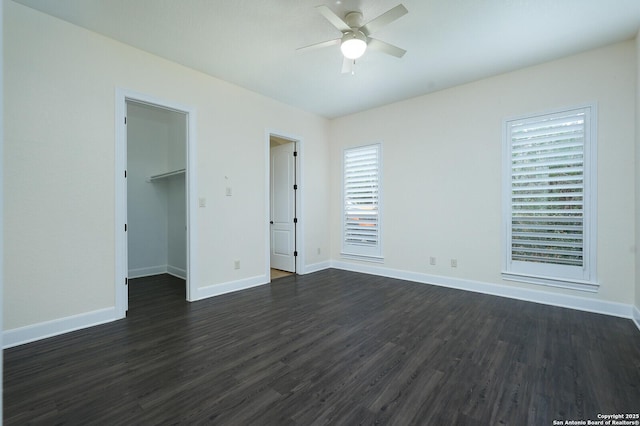 unfurnished bedroom featuring ceiling fan, dark hardwood / wood-style floors, a walk in closet, and a closet