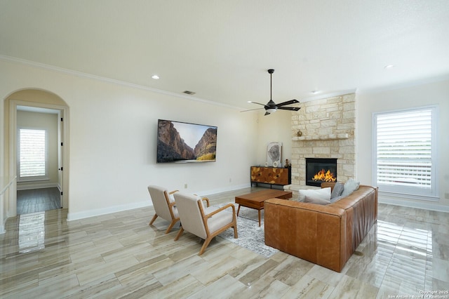 living room with a stone fireplace, ceiling fan, and ornamental molding