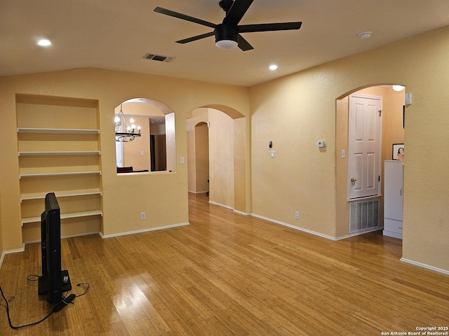 unfurnished living room with built in features, ceiling fan with notable chandelier, and light wood-type flooring