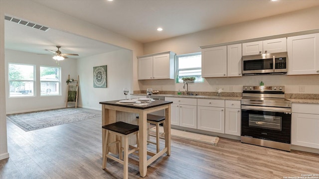 kitchen with white cabinets, appliances with stainless steel finishes, light wood-type flooring, and ceiling fan