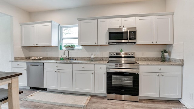 kitchen with light stone countertops, sink, light hardwood / wood-style floors, white cabinets, and appliances with stainless steel finishes