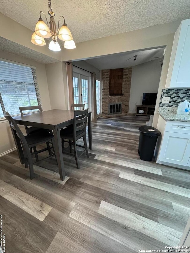 dining area featuring a brick fireplace, a textured ceiling, hardwood / wood-style flooring, and a chandelier