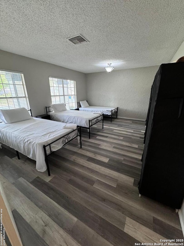 bedroom featuring dark hardwood / wood-style flooring, multiple windows, and a textured ceiling