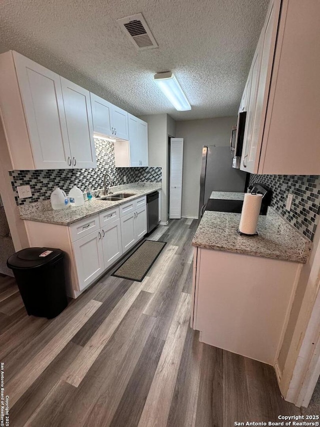 kitchen with dishwasher, wood-type flooring, sink, white cabinetry, and a textured ceiling