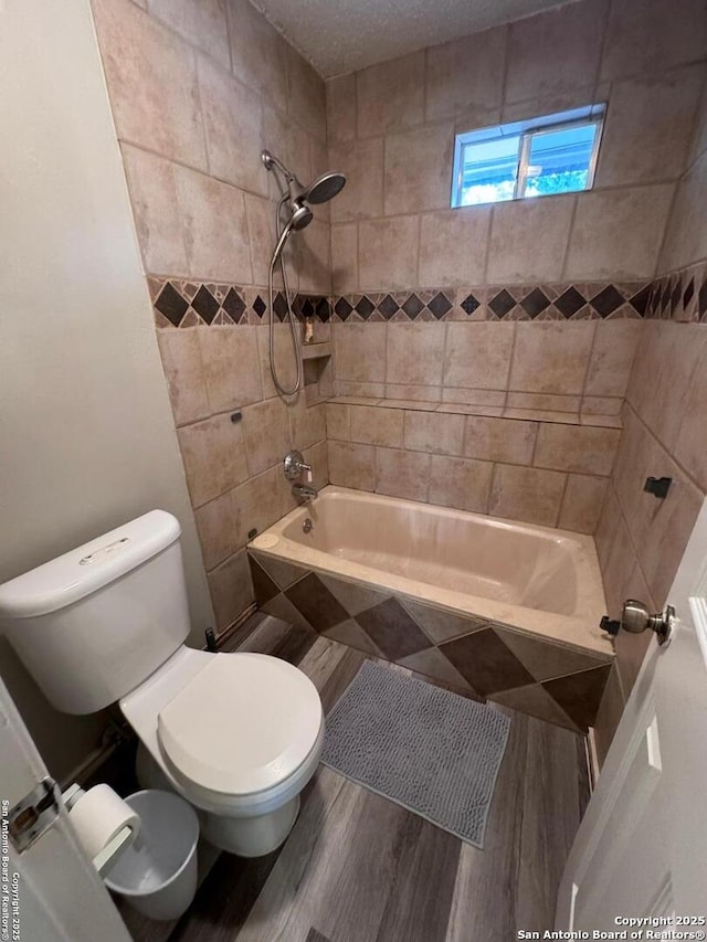 bathroom with toilet, tiled shower / bath combo, wood-type flooring, and a textured ceiling