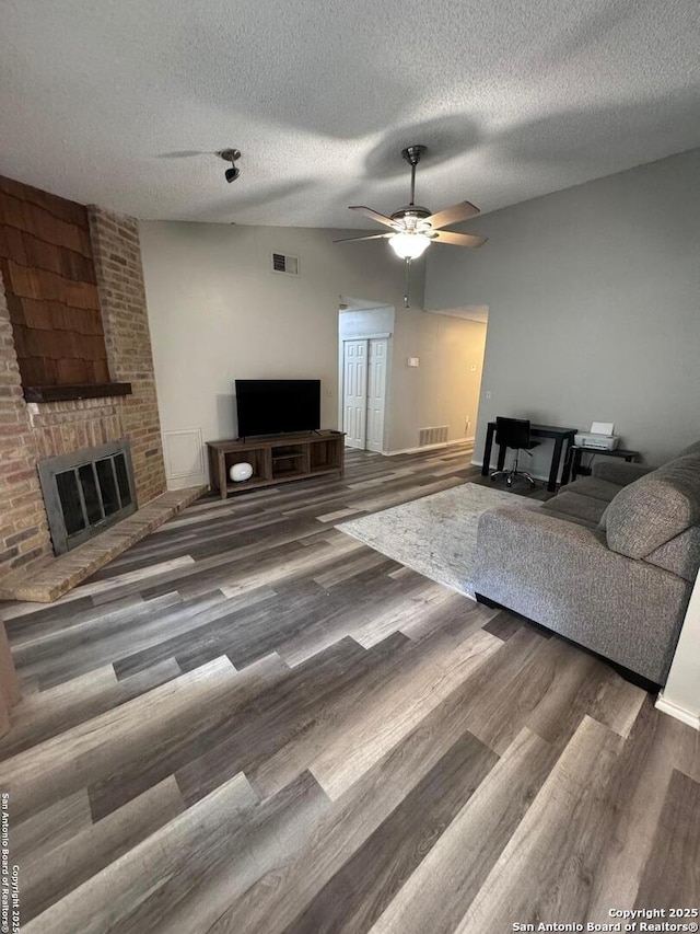 living room with a textured ceiling, lofted ceiling, ceiling fan, dark hardwood / wood-style floors, and a brick fireplace