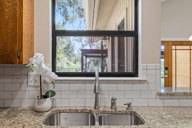 room details featuring backsplash, light stone counters, and sink