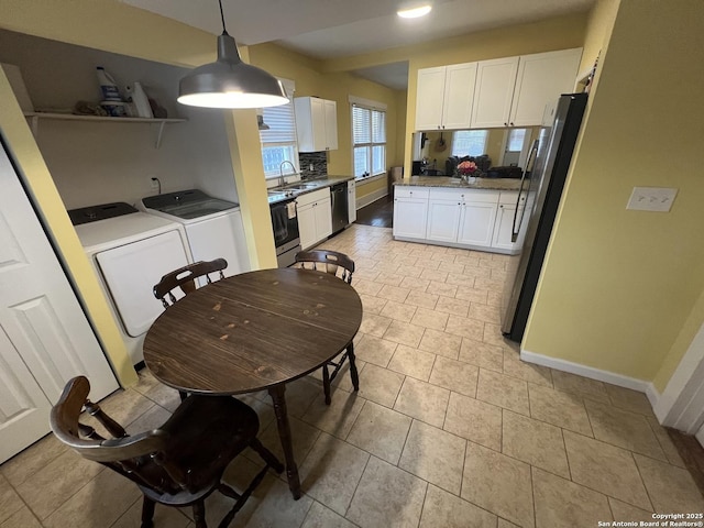 kitchen with sink, independent washer and dryer, appliances with stainless steel finishes, decorative light fixtures, and white cabinetry